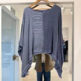 Blusa color azul jean de corte amplio y asimétrico, con diseño bicolor dividido verticalmente, detalles de parches rectangulares con flecos en el pecho y terminaciones deshilachadas.
