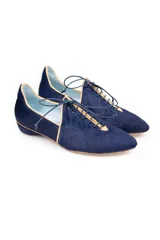 Zapato tipo blucher de pelo pony en color azul marino, con cierre de cordones y ribetes en color ocre. Presenta una silueta geométrica con aberturas laterales y tacón forrado en forma de lágrima.