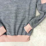 Buzo gris con mangas y cuello rosado claro, confeccionado en algodón rústico.