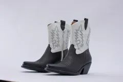 Botas de estilo western (texanas) de caña media, color blanco, confeccionadas en cuero. Presentan bordados decorativos en la caña y puntera cuadrada. Cuentan con cierre lateral y taco de altura media.