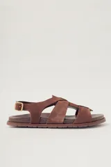 Sandalias planas de gamuza color marrón, con diseño de tiras cruzadas en el empeine y cierre con hebilla metálica dorada en el tobillo. Cuenta con plantilla de cuero y suela de goma con textura.