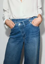 Jeans de tiro medio con diseño wide leg, cintura cruzada y cierre frontal asimétrico con cremallera y botones. Cuenta con cinco bolsillos y presillas para cinto.
