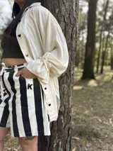 Camisa oversize de fibrana color crudo con botones negros en forma de corazón y mangas largas con puños elásticos.