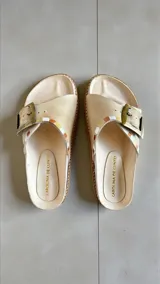 Sandalias de cuero color natural de la marca Carolina de Cunto, con capellada ancha decorada con detalles pintados a mano y una hebilla metálica lateral.