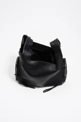 Bolso bandolera de piel vacuna color negro, con estructura blanda y forma hobo o de media luna. Presenta dos bolsillos frontales con cierre metálico plateado y un asa de hombro ancha y ajustable con hebillas y ojales metálicos. El logo de Bimba y Lola está estampado en la parte frontal inferior.