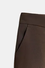 Bermuda de tiro alto en color marrón chocolate, con diseño de corte recto y largo por encima de la rodilla. Presenta pinzas delanteras, bolsillos laterales y cierre frontal con cremallera, botón y gancho.