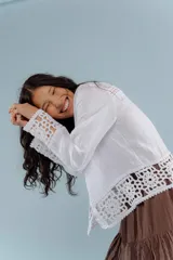 Camisa de lino blanca con detalles de encaje crochet en los puños y en el ruedo. Presenta un diseño romántico con cierre frontal de botones.