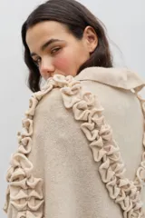 Chal de lana color marrón con diseño envolvente, decorado con volados aplicados en toda la superficie que aportan textura y movimiento.