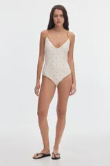 Malla enteriza de color off-white con estampado de lunares negros y vivos en contratono tostado. Presenta escote en V y tirantes finos.