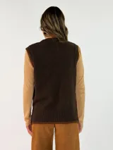 Chaleco de punto en color crema con detalles de ribetes en color marrón oscuro en el cuello, sisas y ruedo. Presenta un diseño clásico con cuello redondo y un pequeño aplique decorativo en el lateral inferior.
