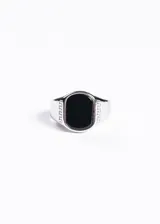 Anillo plateado de acero quirúrgico con piedra negra rectangular en el centro y diseño de grecas en los laterales.