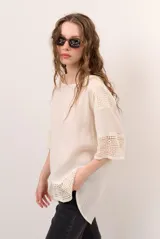 Blusa color blanco, de corte holgado y mangas tres cuartos, con detalles de encaje y bordados en las mangas y en el ruedo.
