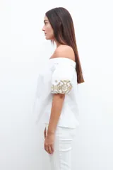 Blusa blanca con escote bardot y mangas cortas abullonadas con bordados dorados.