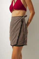 Falda corta tipo pareo con diseño envolvente, confeccionada en tela con estampado de rayas verticales en tonos tierra. Cuenta con un lazo lateral para ajuste y un borde inferior con detalle de costura en contraste.
