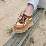 Zapatos de cuero estilo trekking en tonos marrones y beige, con plataforma alta y suela track. Presentan detalles de textura trenzada en los laterales y cordones finos.