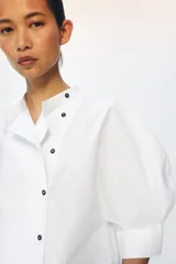Camisa de popelín de algodón con cuello mao y cierre frontal asimétrico con botones a contraste. Presenta mangas cortas abullonadas y bajo recto.