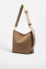 Bolso bandolera de tamaño mediano de la marca Bimba y Lola, color marrón, con exterior de nylon, correa ajustable de lona en tono tostado y detalles de metal dorado. Incluye cierre superior y el logo de la marca estampado en el frente.
