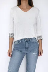 Sweater de tejido de punto color gris, con escote en V y mangas largas. Presenta un diseño liso en el exterior y un detalle de animal print en el interior de los puños, visible al doblarlos.