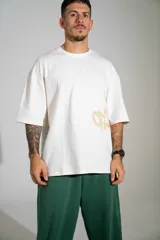 Remera oversize de algodón color off-white, con mangas cortas amplias y cuello redondo. Presenta un pequeño estampado en el centro del pecho y un diseño gráfico más grande en el lateral inferior.