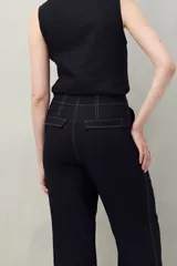 Pantalón negro de corte recto y tiro alto, confeccionado en denim con costuras a contratono en color blanco. Presenta bolsillos frontales tipo parche y cierre frontal con botón y cremallera.