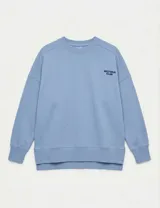 Buzo de cuello redondo en color celeste, con diseño de hombros caídos y bordado pequeño en el pecho con la frase 'UNIFORM CLUB'. Presenta puños y ruedo acanalados, con un corte ligeramente más largo en la parte posterior.