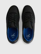 Zapatillas urbanas Calvin Klein con diseño de corte bajo. Presentan una combinación de materiales en la capellada, incluyendo paneles de nailon, cuero y ante en color negro. Destacan por su suela de goma blanca con el logo de la marca estampado en el lateral, forro interior en color azul vibrante y cierre mediante cordones.