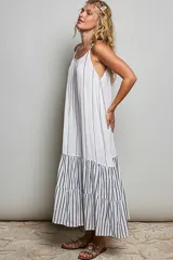 Vestido largo sin mangas de color blanco con rayas verticales oscuras, corte holgado y diseño con volantes en la parte inferior.