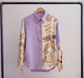 Camisa blanca con estampado de hojas en tonos beige y verde, cuello camisero, mangas largas con lazos en los puños y botones de madera.