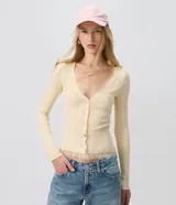 Cardigan de tricot acanalado color beige, de calce ajustado, con mangas largas y escote en V. Cuenta con cierre frontal con botones y detalles de encaje aplicado en el escote y el ruedo.