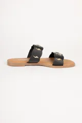 Sandalias bajas de símil cuero color negro con suela marrón y doble tira ancha decorada con apliques metálicos dorados de forma orgánica.