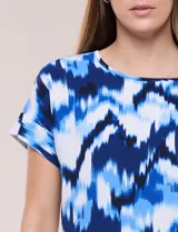 Blusa de silueta holgada y recta, confeccionada en crepe de poliéster con estampado animal print. Presenta escote redondo clásico, mangas cortas de hombro caído con puño doblado y ruedo ligeramente curvo.