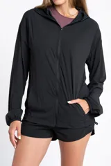 Campera deportiva de color negro con cierre frontal, capucha y mangas largas con puños elásticos. Presenta una textura ligera y un corte ajustado al cuerpo.