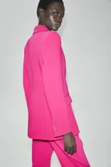 Blazer cruzado fucsia con cuello solapa, manga larga, bolsillos con solapa en el delantero y cierre frontal con botones forrados.