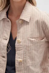 Chaqueta cropped de manga larga, color blanco con finas rayas verticales en tono claro. Presenta cuello camisa, cierre frontal con botones de madera y dos bolsillos delanteros con tapa a la altura del pecho.