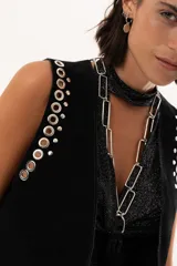 Chaleco negro de gamuza con diseño sin mangas, decorado con ojales metálicos plateados a lo largo de los bordes frontales y sisas.