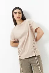 Remera oversized de algodón color beige claro, con cuello redondo y cordones ajustables a los costados que crean un efecto de lazada.