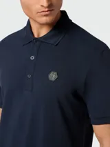 Polo de piqué azul marino con cuello clásico, tapeta de botones y logo metálico en el pecho.