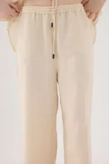 Pantalón de lino color beige, de silueta relajada, tiro medio-alto, cintura elastizada con cordón ajustable, bolsillos laterales y bolsillos traseros.
