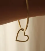 Pulsera tipo aro rígido de metal color bronce, con un dije colgante con forma de corazón calado.