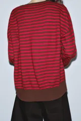 Jersey de punto con diseño a rayas horizontales en color rojo y marrón. Presenta cuello redondo, manga larga con puños ajustados y ruedo acanalado.