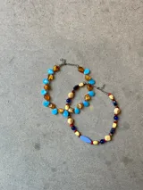 Gargantilla corta hecha a mano con mix de cuentas de cristal en forma de gota, alternando tonos celestes y ámbar, con terminaciones y cadena de extensión en acero.