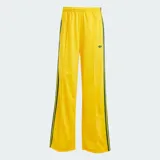 Pantalón deportivo Adidas de corte holgado, color amarillo brillante con las clásicas tres tiras verdes en los laterales y el logo del trifolio bordado en la pierna izquierda. Cuenta con cintura elástica y bolsillos laterales con cierre.
