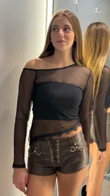 Short de cuero sintético color marrón chocolate, con diseño de tiro bajo y cierre frontal mediante cordones entrelazados con ojales metálicos. Presenta detalles de tachas y argollas metálicas en la parte frontal.