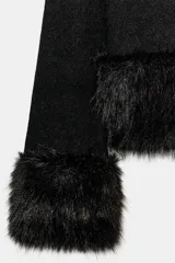 Chaqueta de punto negra de manga larga y cuello redondo, con detalles de pelo sintético en el bajo y los puños. Cuenta con cierre frontal con botones a presión ocultos.