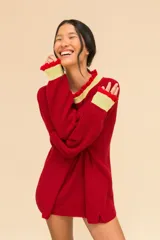 Buzo de punto oversize color rojo, con cuello alto y puños con terminaciones en volados. Presenta detalles en contraste color amarillo en el cuello y los puños, con un tejido de acabado ligeramente brillante.