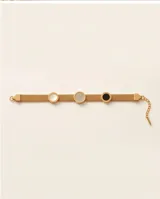 Pulsera rígida de acero con baño dorado, de diseño mallado, con tres dijes circulares incrustados con detalles en ónix, nácar y circonias.