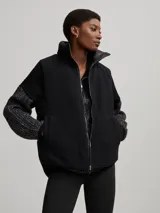 Chaleco negro capitoneado con cuello de piel sintética y cierre frontal con cremallera. Diseño sin mangas y corte recto.