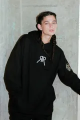 Buzo negro oversize de frisa con capucha amplia, bolsillo canguro, terminaciones de puño y ruedo con rib, y logo bordado en el centro delantero.