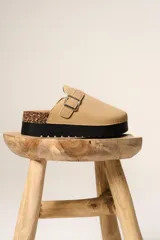 Zueco de plataforma color beige, con capellada de gamuza sintética, detalle de hebilla metálica lateral y suela de goma negra con detalle de corcho en el talón.