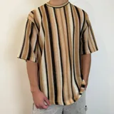 Remera de tejido de punto con diseño de rayas verticales en tonos tierra, negro y crema. Presenta un corte oversize con cuello redondo y mangas cortas.